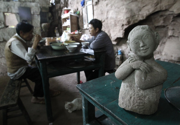 Peng Fuquan, 69, and his wife have lunch near a stone sculpture they created inside a cave excavated by the couple in a fissure at a cliff wall in a remote area of the Southwest China city of Chongqing on July 11. Couple's 17 years of seclusion at cave