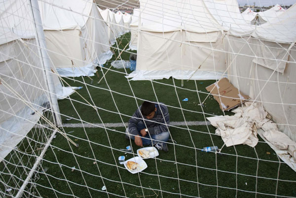 A man eats his meal on a soccer pitch at a stadium used as a relief shelter campsite for earthquake victims in Ercis Oct 26, 2011. Turkey struggles to shelter people after quake