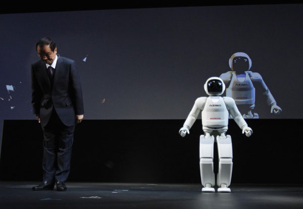 Honda Motor Company President Takanobu Ito (L) bows next to the company's Asimo humanoid robot during a news conference at the 42nd Tokyo Motor Show in Tokyo November 30, 2011. Tokyo Motor Show kicks off