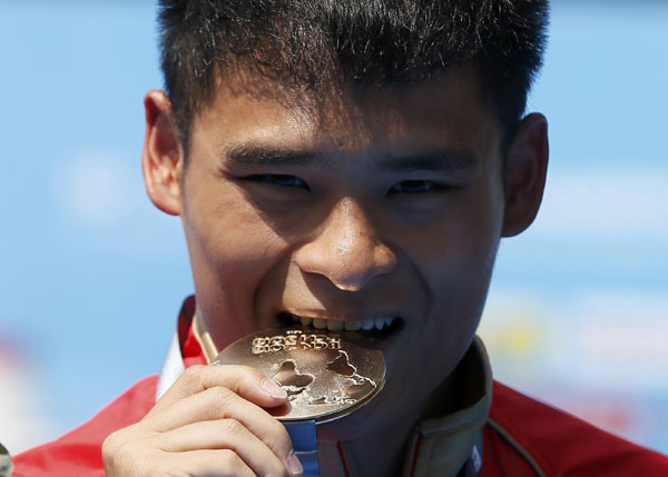 China's Li Shixin bites his gold medal as he poses at the men's 1m springboard victory ceremony during the World Swimming Championships at the Montjuic municipal pool in Barcelona, July 22, 2013. China wins one more gold at World Championships