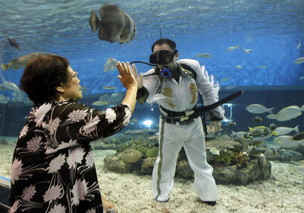 A visitor gives a high five to a professional diver wearing an Elvis Presley attire inside an aquarium of the Ocean Park in Manila August 15, 2011. Presley, the 'King of Rock and Roll', died at his home, Graceland Mansion, in Memphis, Tennessee, at the age of 42 on August 16, 1977 from drug overdose. Fans remember Elvis Presley
