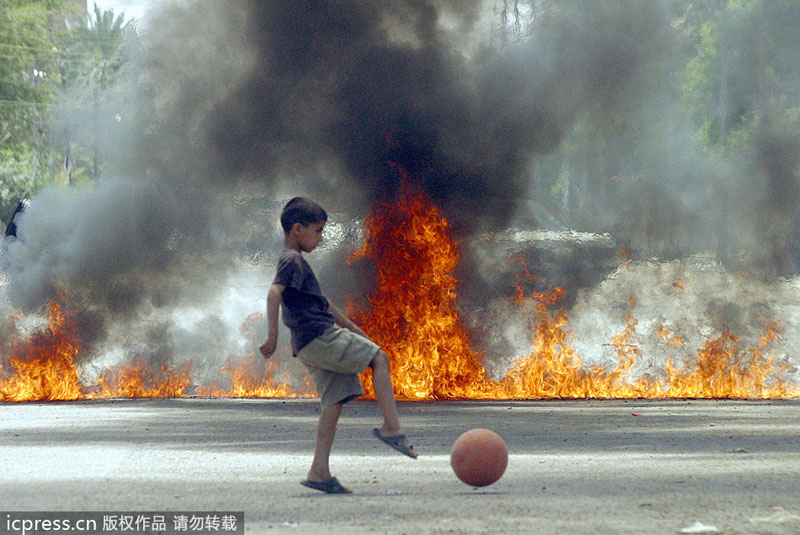 An Iraqi boy plays in front of flames blocking a street in Baghdad's Shiite Sadr City neighborhood, on May 18, 2004. Public sports in post-war Iraq