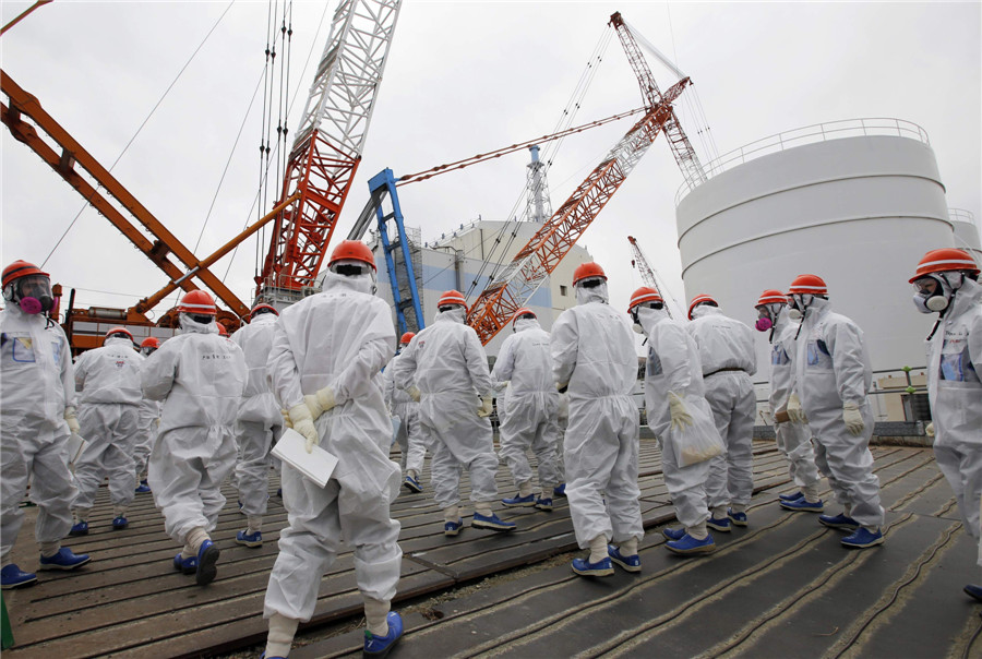 Members of the media and Tokyo Electric Power Co. (TEPCO) employees wearing protective suits and masks walk toward the No 1 reactor building at the tsunami-crippled TEPCO's Fukushima Daiichi nuclear power plant in Fukushima prefecture March 10, 2014. Visit to Fukushima nuclear plant on meltdown anniversary